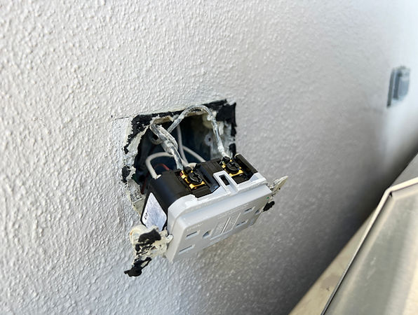 A white wall featuring a black electrical outlet and a white light switch positioned above it.